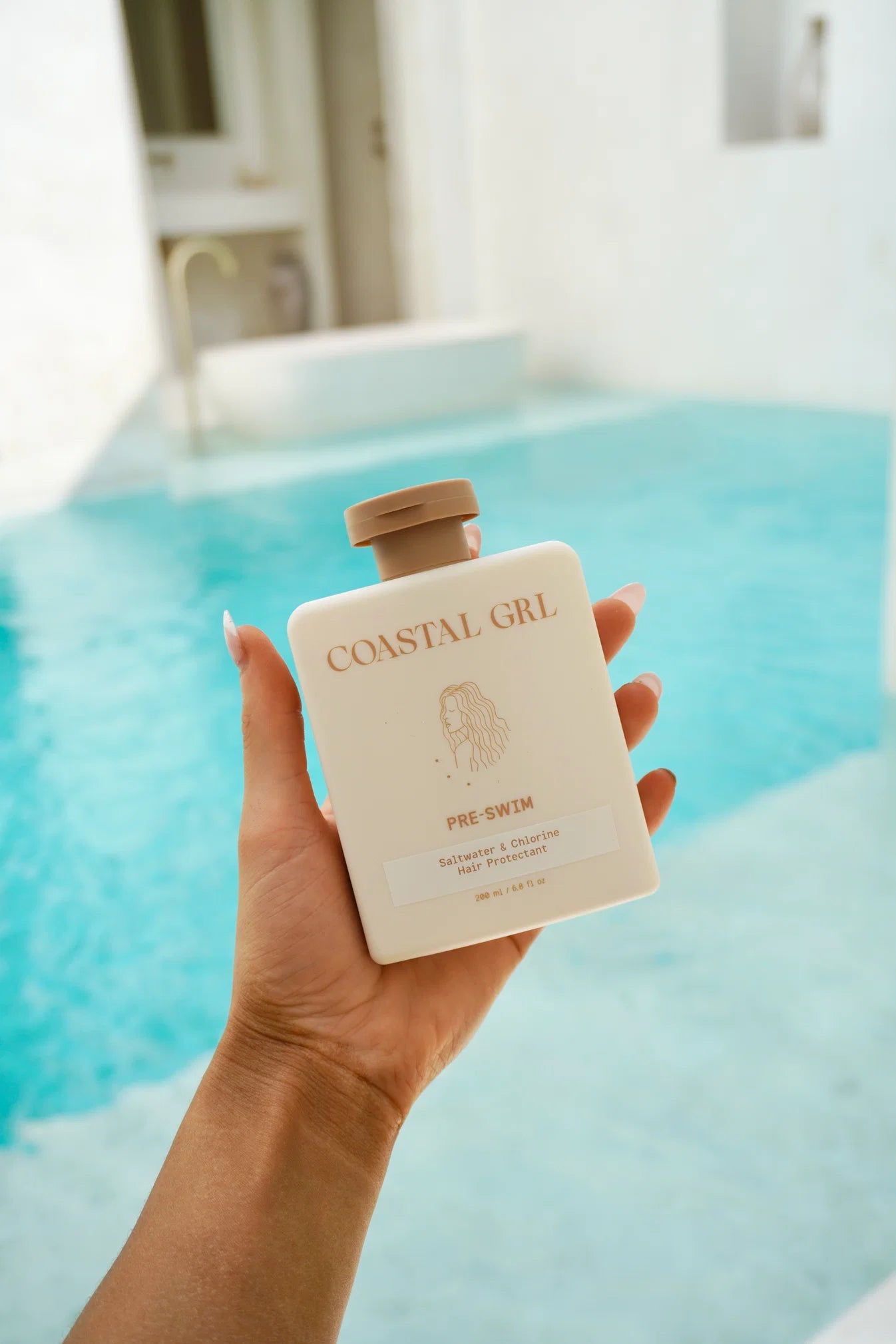 Hand holding a bottle of 'Coastal Girl' product by a pool