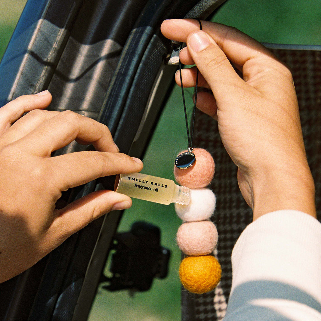 Person hanging a decorative car air freshener with beads on a car's rearview mirror.
