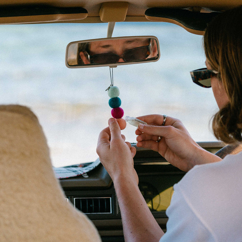 Person in a car holding a colorful car charm near the rearview mirror.