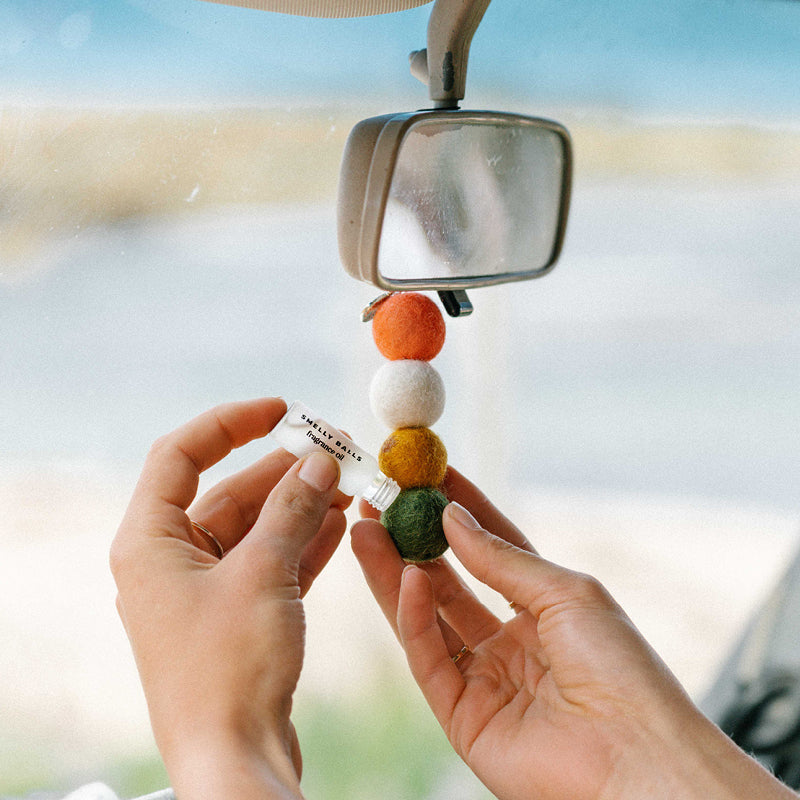 Colorful keychain with beads held by hands in front of a car's rearview mirror.